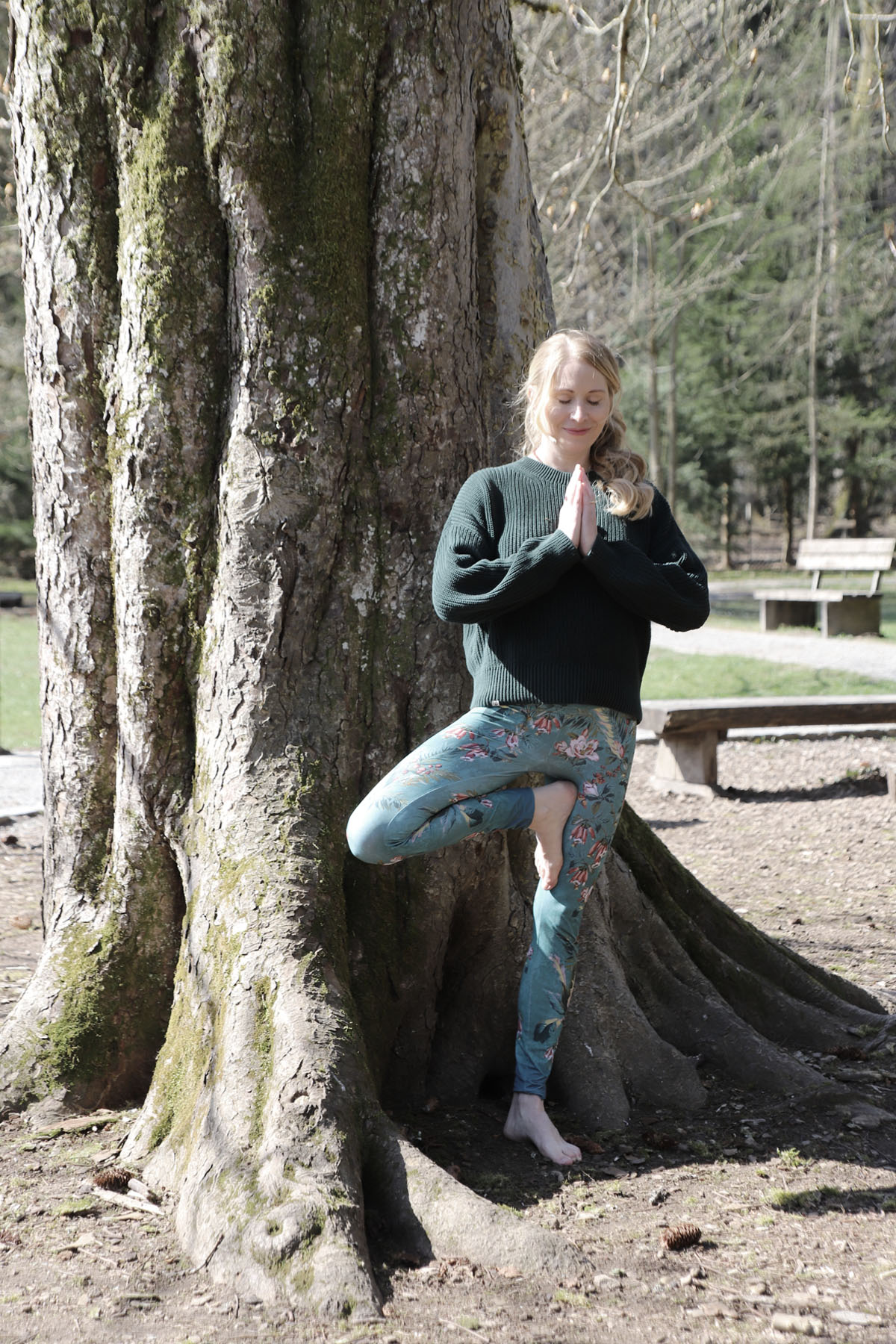 Nathalie Koschik, Body Mind Memories Nathalie Koschik von Body Mind Memories in der Yogahlatung "Der Baum" vor einem Baumstamm, sie lächelnd mit geschlossenen Augen